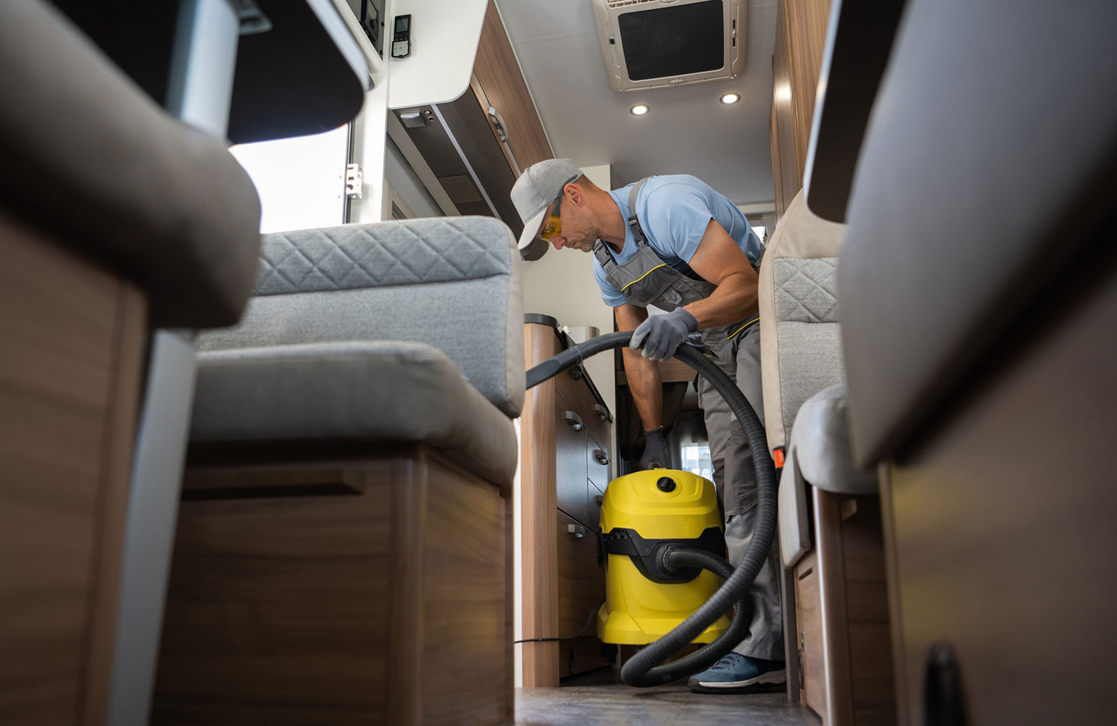 An employee in overalls cleans an RV interior after a pre-trip inspection to ready it for a trip from the storage facility to the owner's destination.