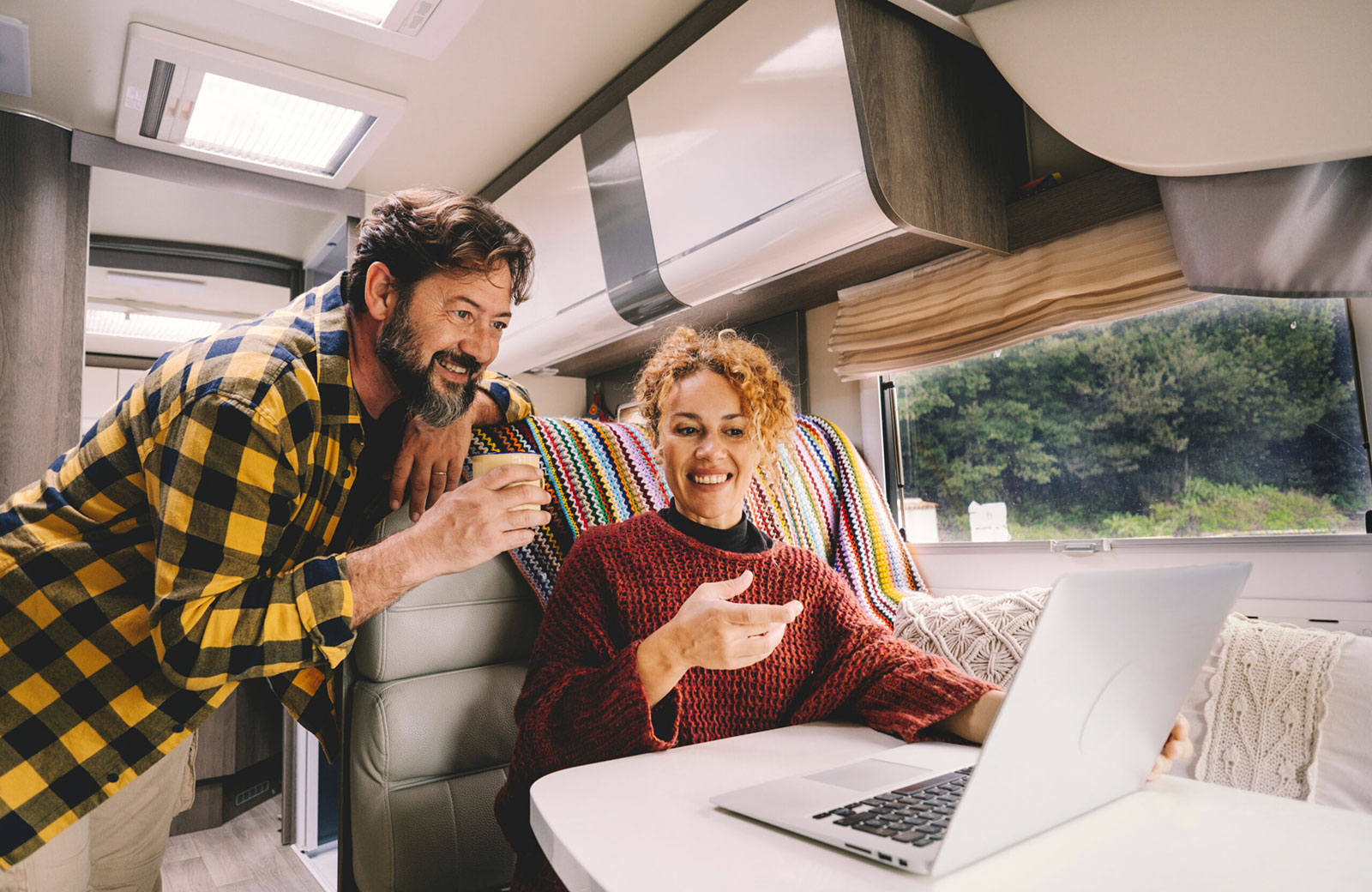 Couple relaxes inside of their luxury RV in bright fall colored clothing, while checking their laptop on vacation after an easy adventure launch from Waypoint Storage.