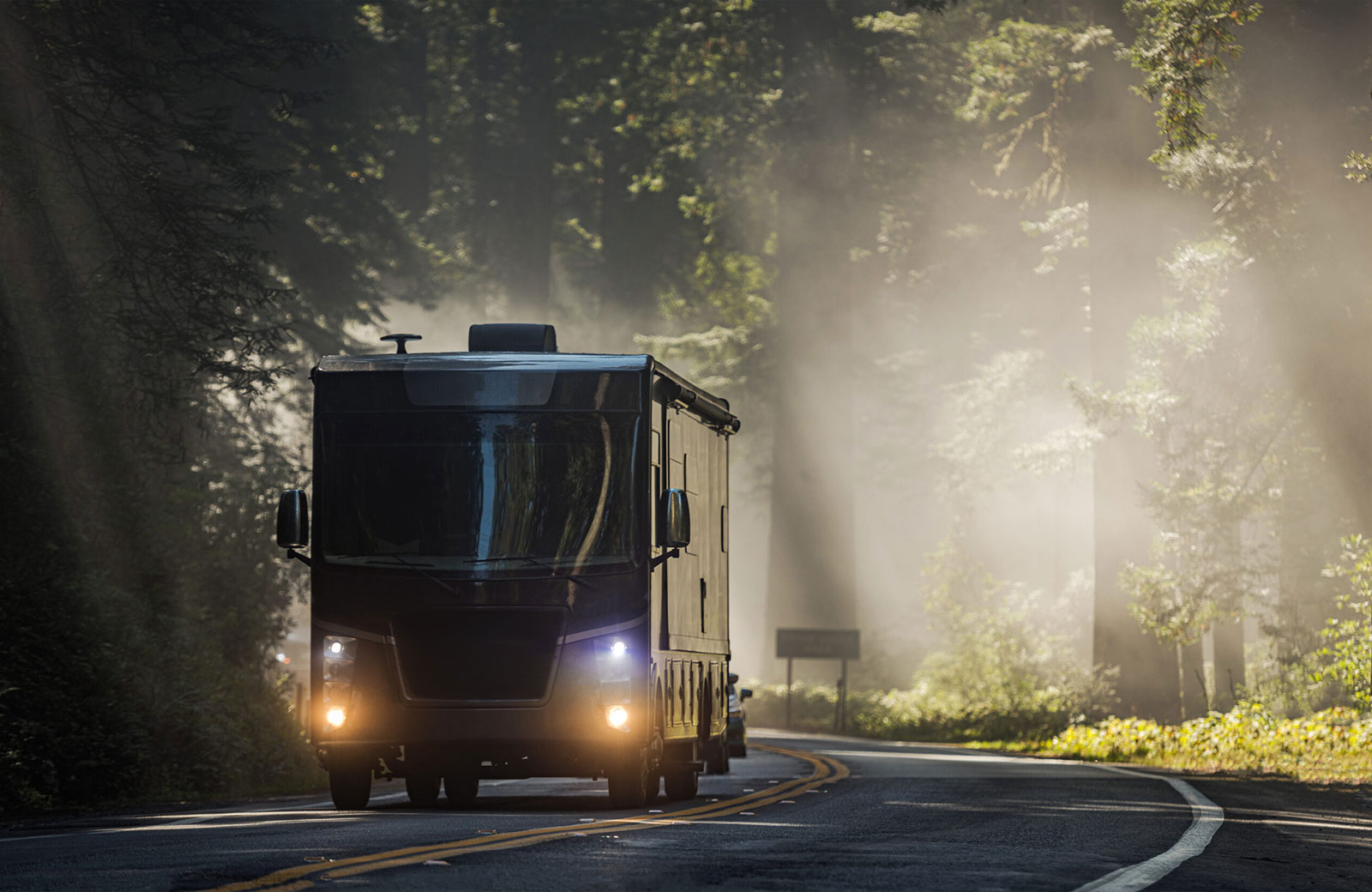 An RV, also known as a motorhome, travels a beautiful scenic route in the fog through a forest.
